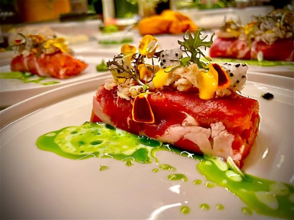 Gepresenteerd gerecht met rauwe ham, garnalen en een groene saus.